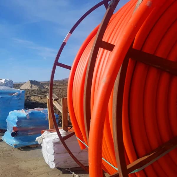 Roll of orange HDPE conduit on job site with pallets of elbows in the background